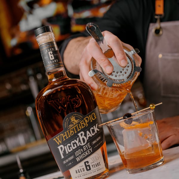 A bartender pours WhistlePig PiggyBack 100% Rye Whiskey from a shaker into a glass with ice and garnish.