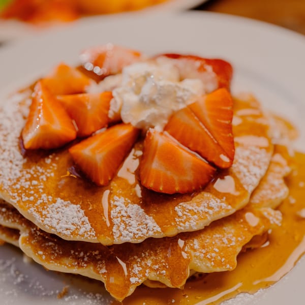 Stack of pancakes with strawberries, whipped cream, powdered sugar, and maple syrup.