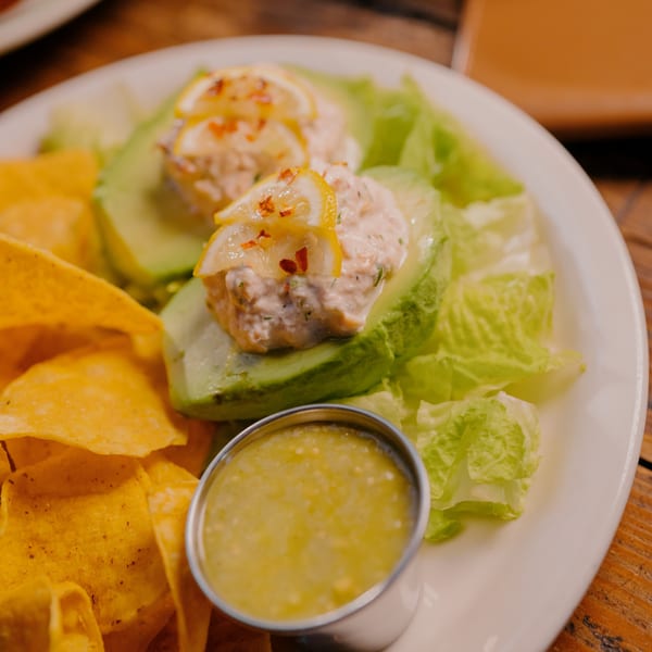 Avocado halves filled with creamy seafood salad, topped with lemon slices and chili flakes, served with tortilla chips and salsa verde.