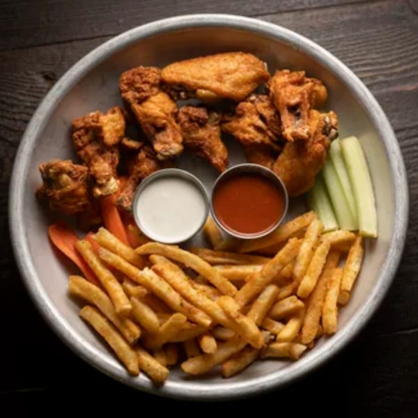 A metal platter of Brasserie Saint James' crispy chicken wings, fries, celery, carrots, and dipping sauces.