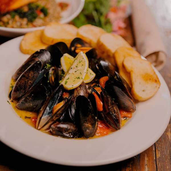Steamed mussels in a savory broth with lemon wedges and toasted bread on a white plate.