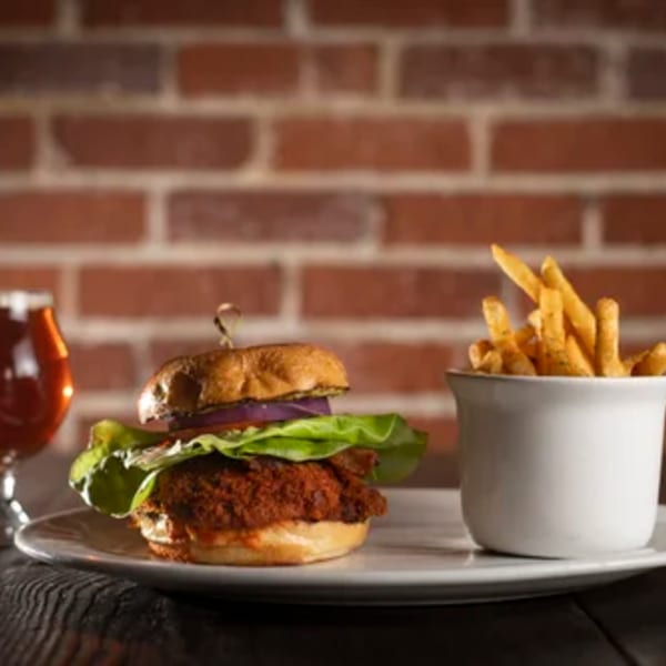 Brasserie Saint James' fried chicken sandwich with lettuce, onion, and fries, alongside a beer.