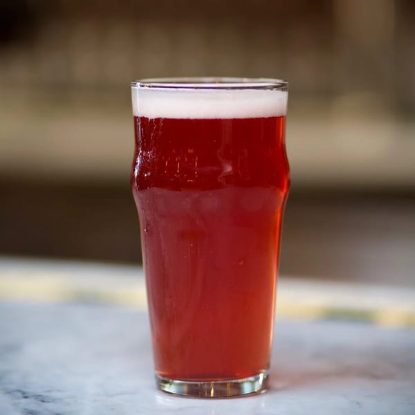 A pint glass of Brasserie Saint James' red brew, topped with a frothy white head.