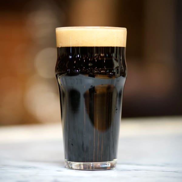 A pint glass of dark Brasserie Saint James brewpub beer with a thick, creamy head.